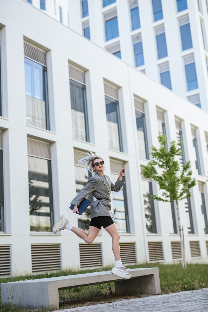Woman with tablet in stylish suit jumping holding sunglasses