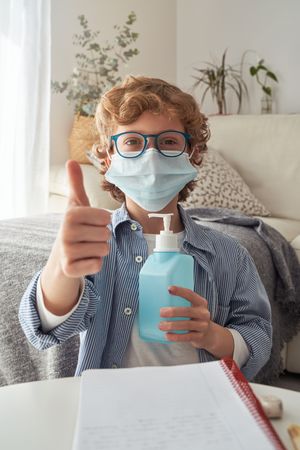 Boy in mask and with sanitizer showing thumb up