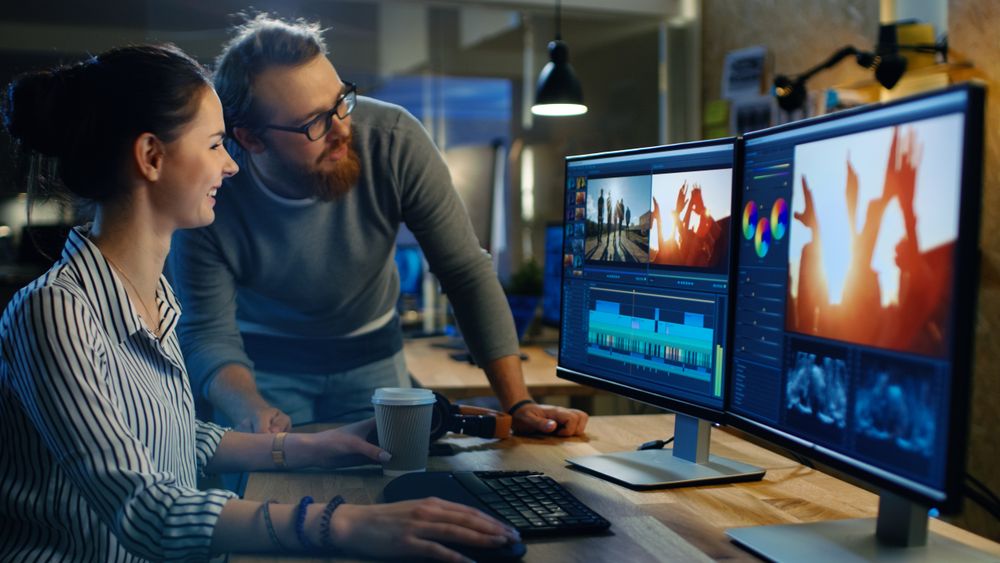 Female Video and Sound Editor Works With Male Colleague on a Project on Her Personal Computer with Two Displays.