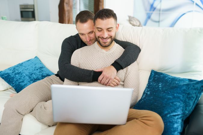 Male couple chilling on sofa with laptop