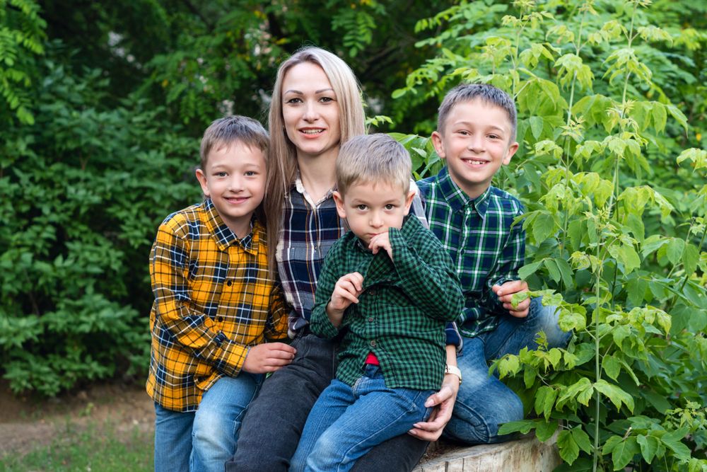 Single parent family with three children sitting on tree stump leaning on mother