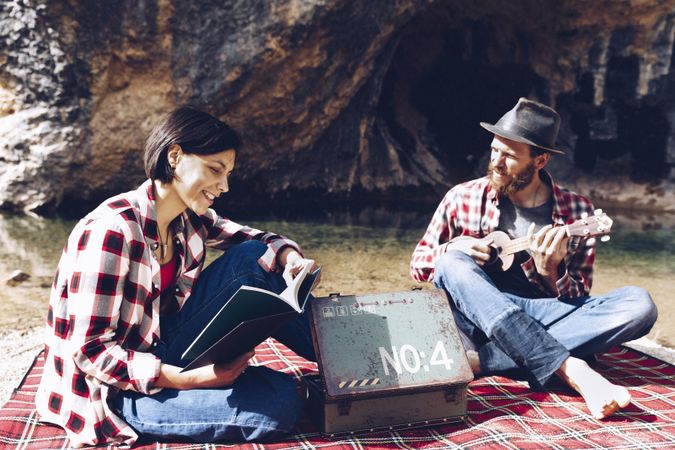 Chilling couple with book and guitar on shore