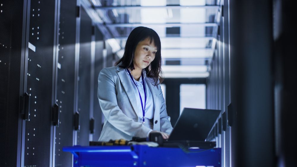 Asian Female IT Engineer Working on a Laptop on Tool Cart, She Scans Hard Drives.