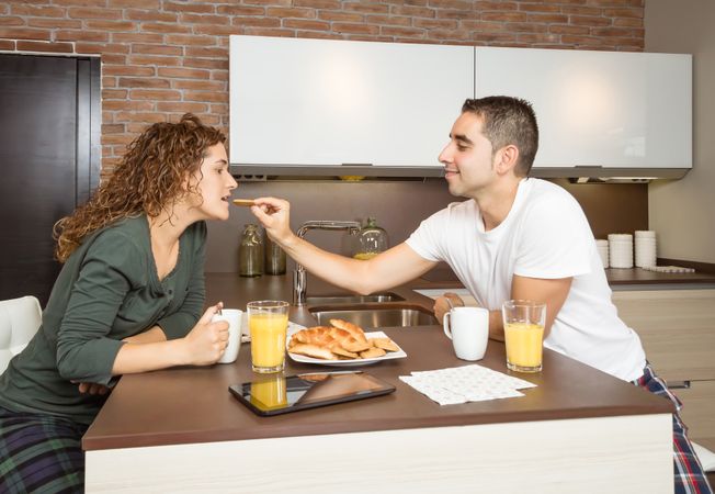 Man affectionately feeding woman breakfast of pastries