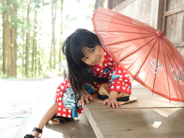 Girl  wearing kimono and holding umbrella sitting outdoor