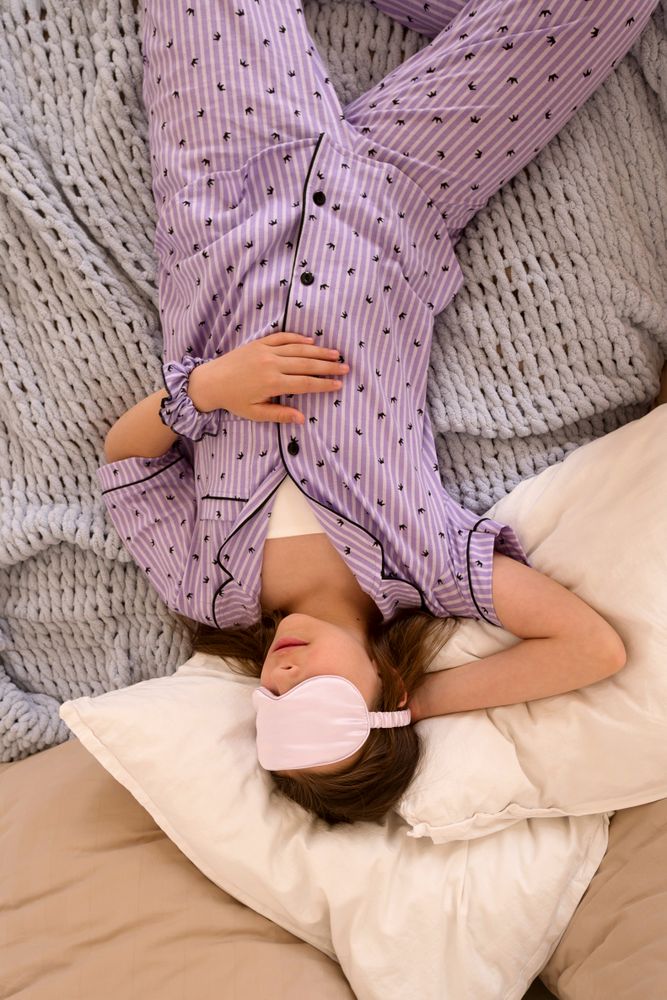 Girl lying upside down on bed with sleep mask.