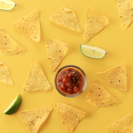 Chips, salsa and lime artfully scattered on yellow background