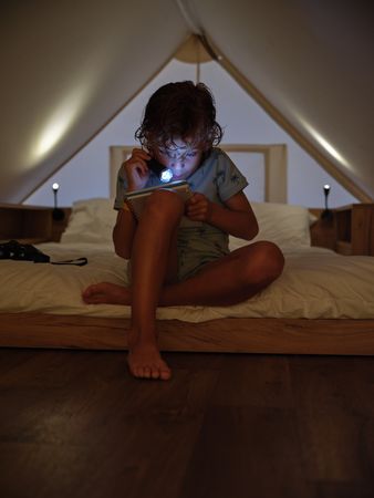 Concentrated boy reading book with flashlight