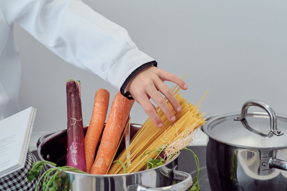 Crop preteen boy adding spaghetti into saucepan while preparing