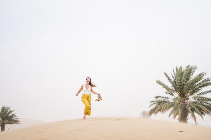 Happy woman holding shoes in desert