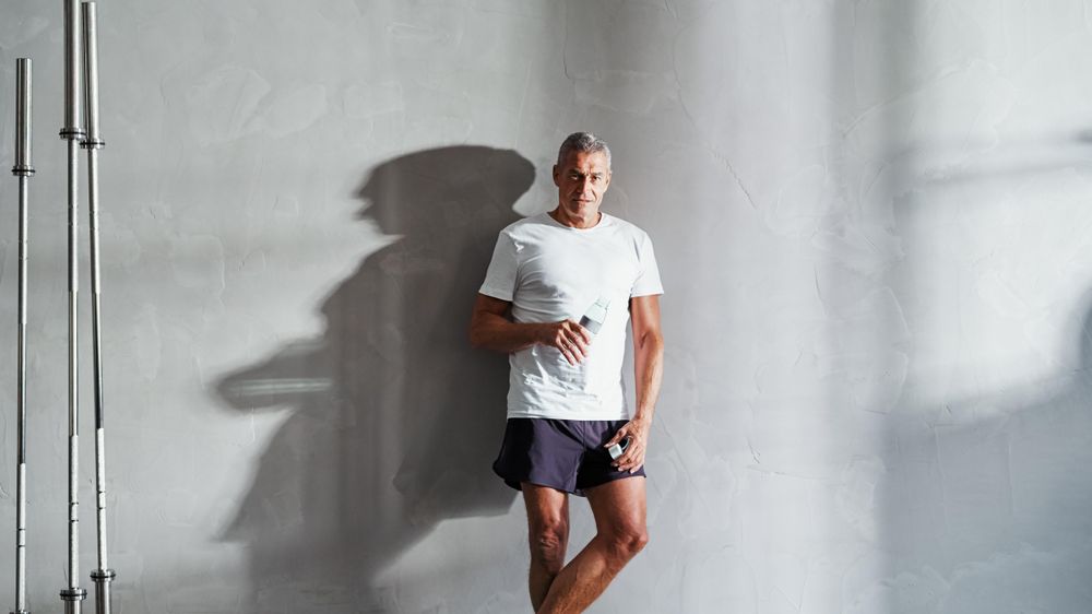 Man standing against the wall with water after exercising with water bottle