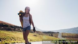 Happy young woman walking with a longboard on countryside road 4j7MRb