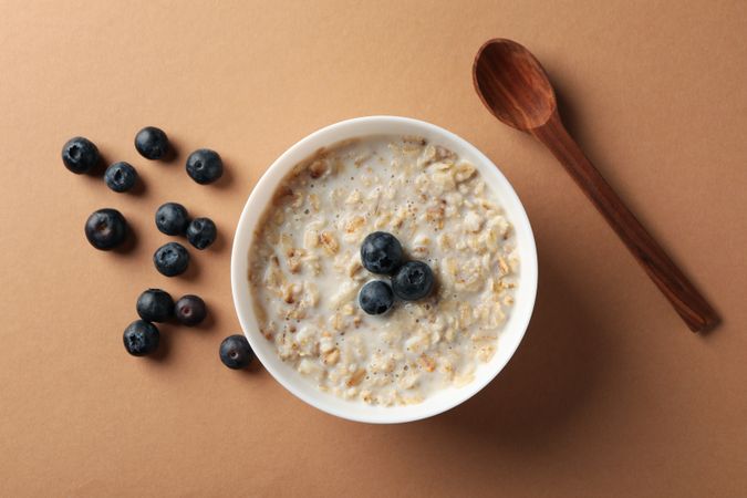 Spoon and bowl with oatmeal porridge and berry on craft background