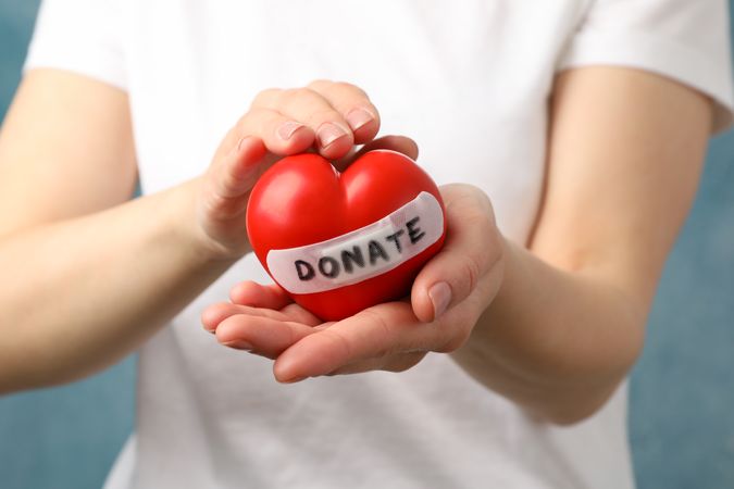 Woman holds heart on blue background, close up. Health care, organ donation