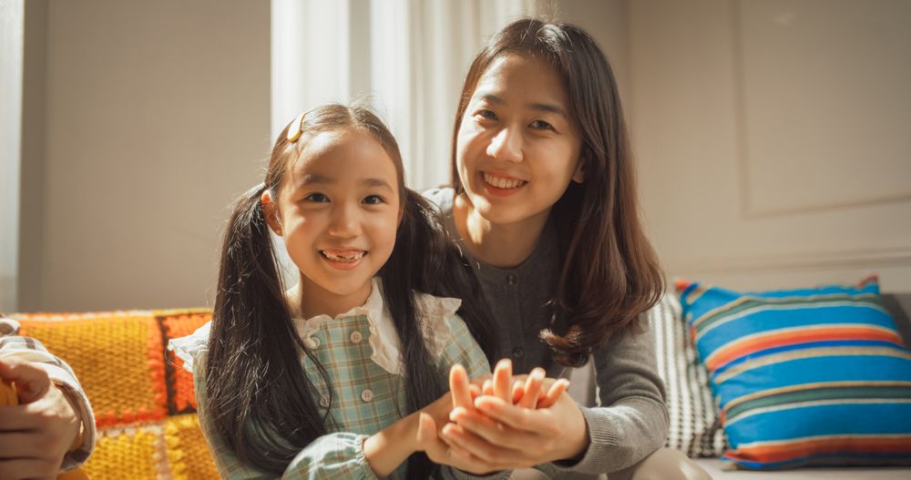 Portrait of a Happy Korean Mother and Cute Daughter at Home, Smiling and Waving at the Camera.