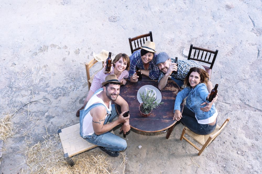 Aerial view of a group of friends sitting around a table holding beers with copy space