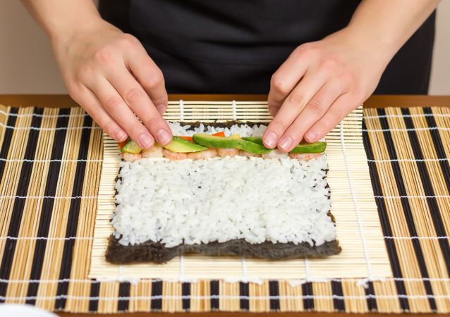 Hands of woman chef arranging filling in rice to roll sushi in a nori seaweed sheet