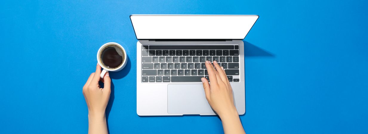 Looking down at person using laptop in a blue room with coffee with blank screen with copy space