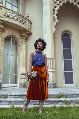 Woman in blue shirt and brown skirt holding a handbag outdoor