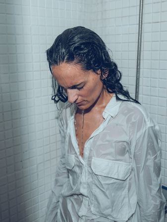 Fatigue female in wet white shirt standing under pouring shower