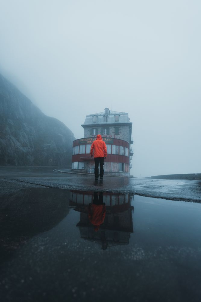 Back view of person in orange jacket standing facing a store on a rainy day