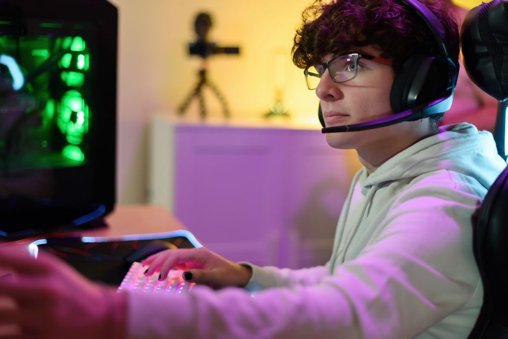 Young man in headphones playing on keyboard and sitting at table with gadgets
