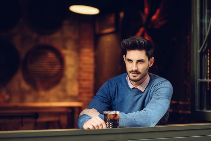 Man in sweater sitting with drink in modern pub