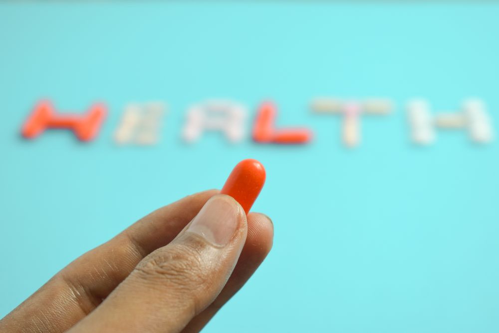 Person holding pill in front of "HEALTH" spelled on blue table