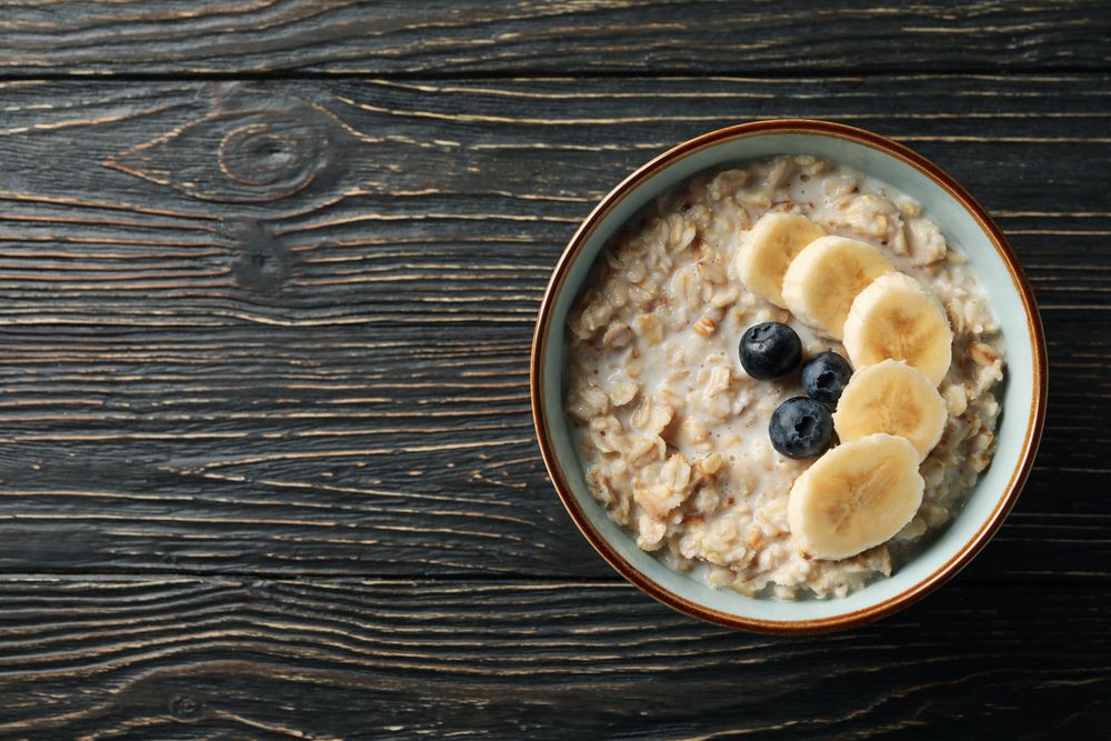 Bowl with oatmeal porridge and fruits on wooden background