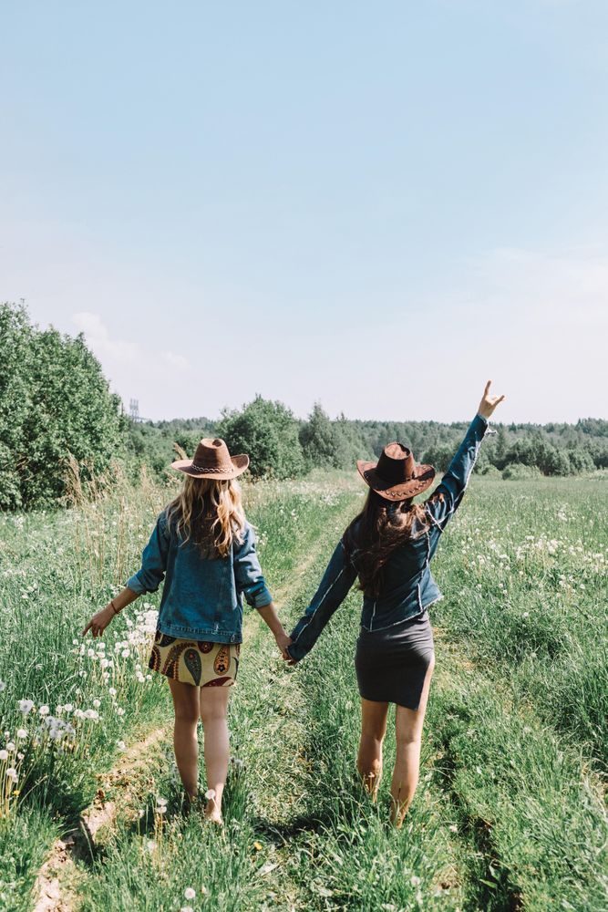 Two women wearing hats and holding hands and walking on grass field
