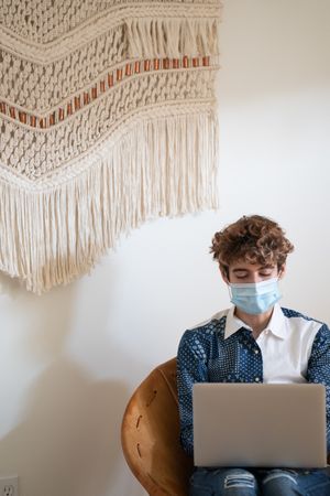 Nonbinary person sitting with a laptop wearing a face mask