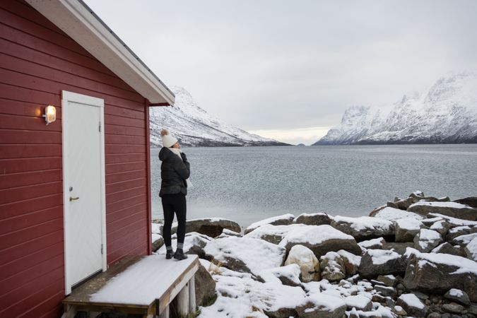 Solitary woman on rocky shore against tranquil lake and snowy mountains in cold day