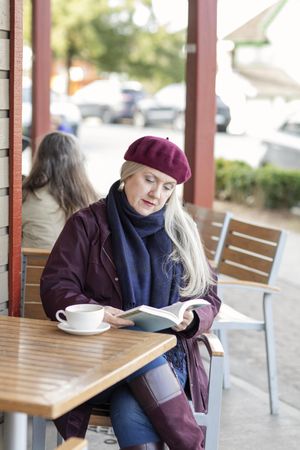 Woman reading book while sitting at an outdoor table at a coffee shop.