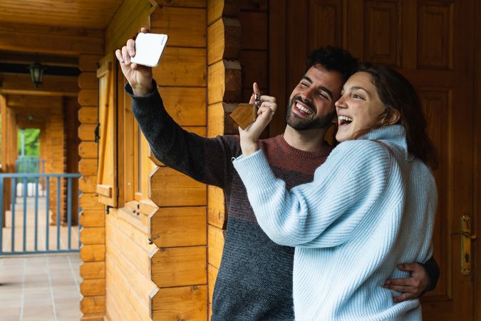 Delighted couple with keys of new house taking selfie on terrace