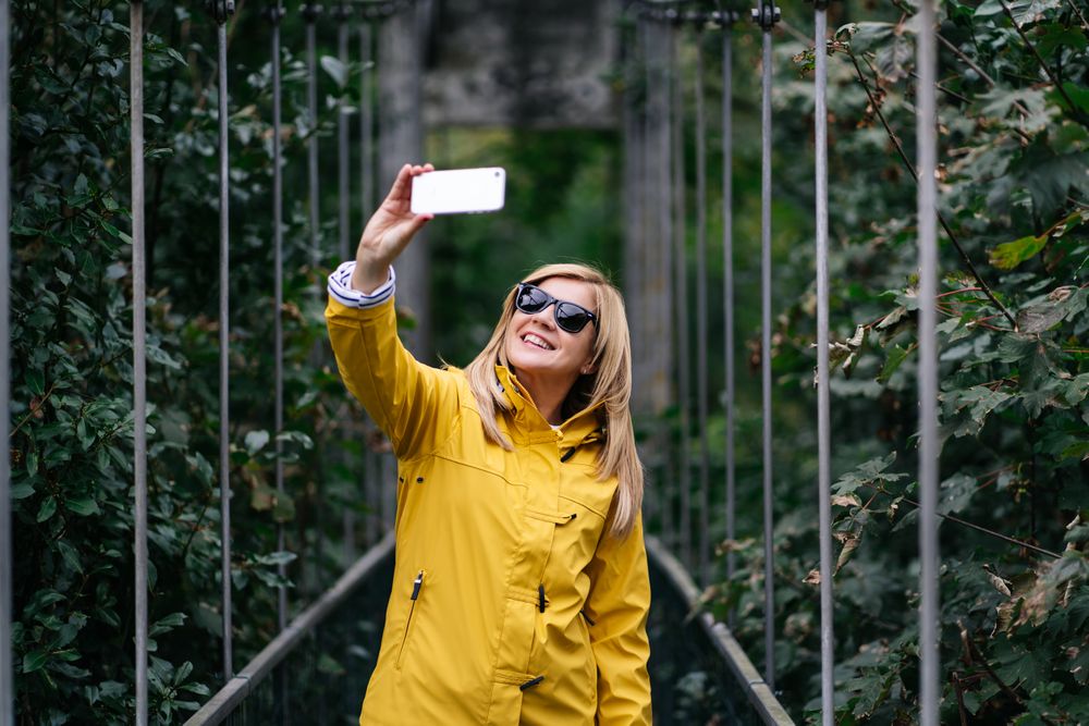 Happy female traveler taking selfie on suspension bridge in summer