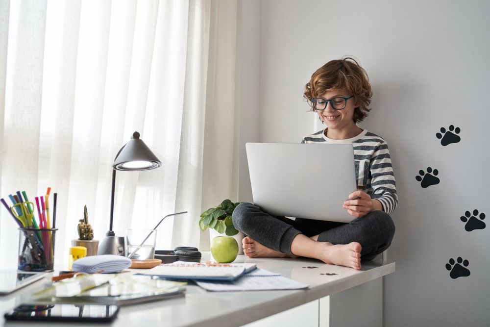 Happy barefoot boy looking at screen and using laptop at home
