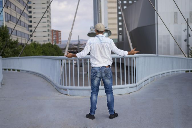 Male in denim standing with open arms on bridge above city