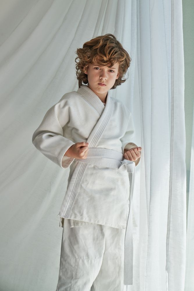 Confident preteen kid in kimono practicing karate near window