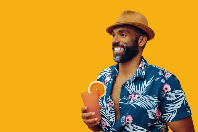Male holding a drink while wearing colorful shirt with yellow background, copy space