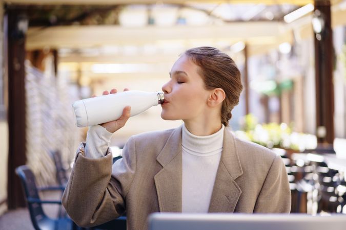 A Stylish Young Woman is Relishing a Refreshing Drink While Seated Outdoors at a Cozy Cafe
