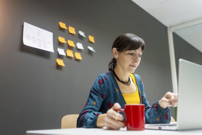 Businesswoman with hot beverage using laptop