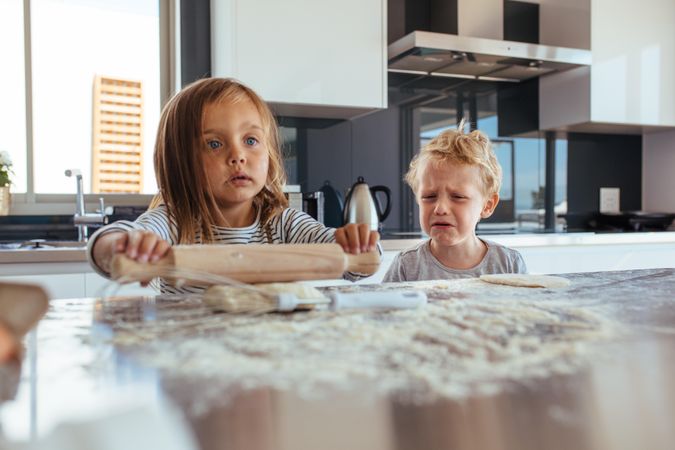 Cute little girl preparing a dough for cookies and little boy crying standing by