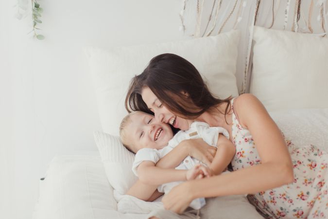 Mother ticking little son and laughing on bed
