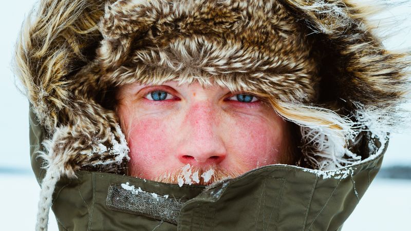 Close-up of man with blue eyes wearing parka jacket and covered with snow