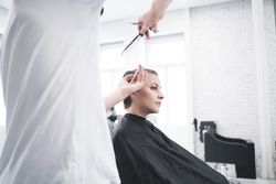 Hairdresser cuts woman's hair with scissors