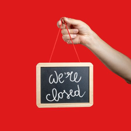 Hand holding a "We're closed" sign on a red background.