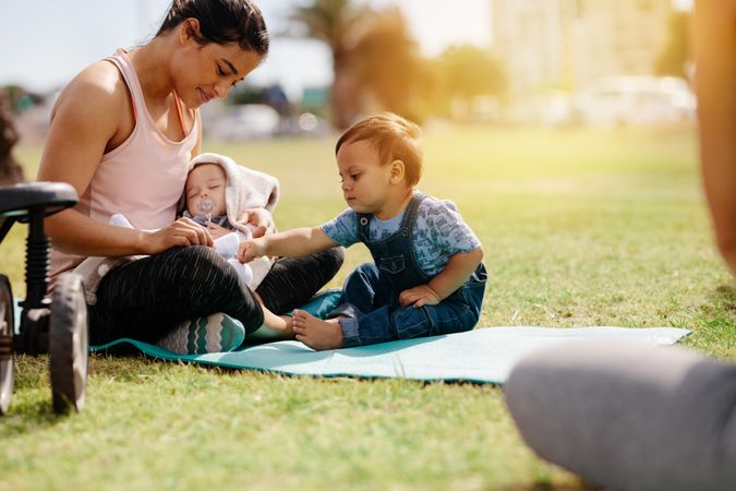 Young mom in fitness wear sitting in park with her kids