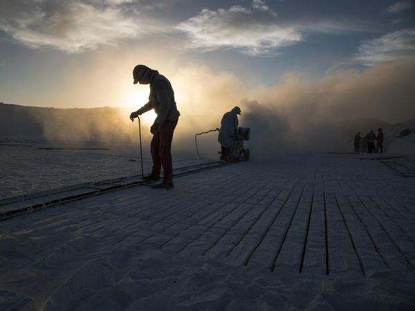 Group of workers flattening sand base at sunset