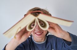 Cheerful boy looking at camera through opened book