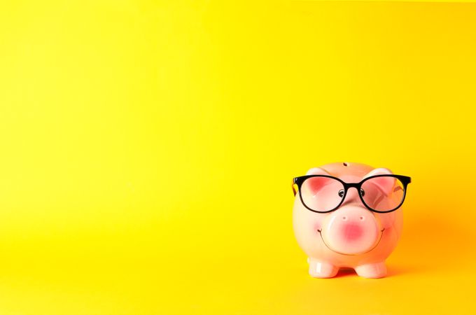 Happy piggy bank with glasses on yellow background, space for text. Finance, saving money